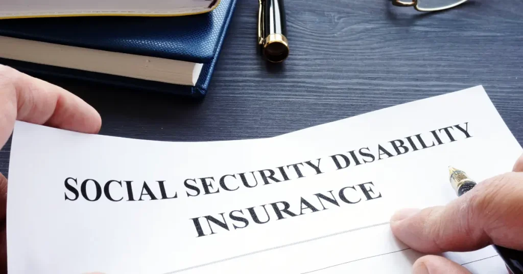 A person holds a document titled “Social Security Disability Insurance” with a pen nearby